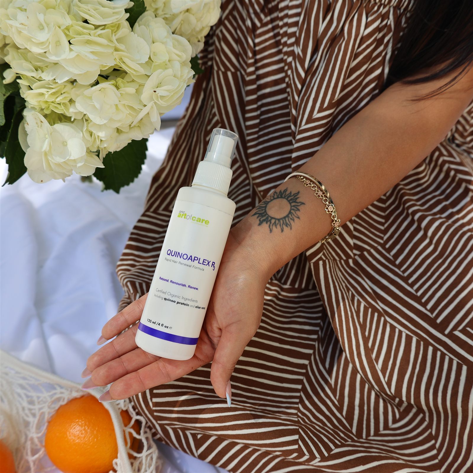 Hair care product held in front of striped fabric and flowers